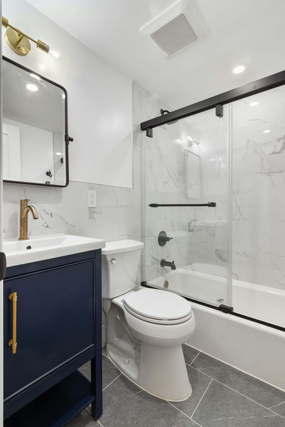 Moderne badkamer met marineblauw badmeubel, gouden kraan en marmeren tegels.